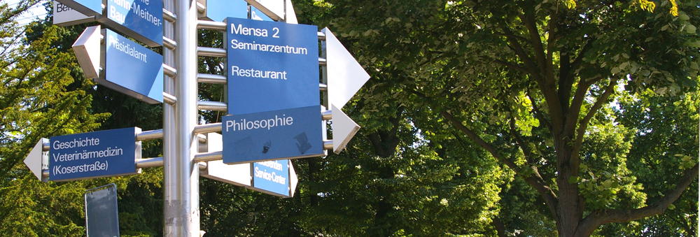 Ein Wegweiser mit mehreren Schildern auf dem Gelände der Freien Universität Berlin.