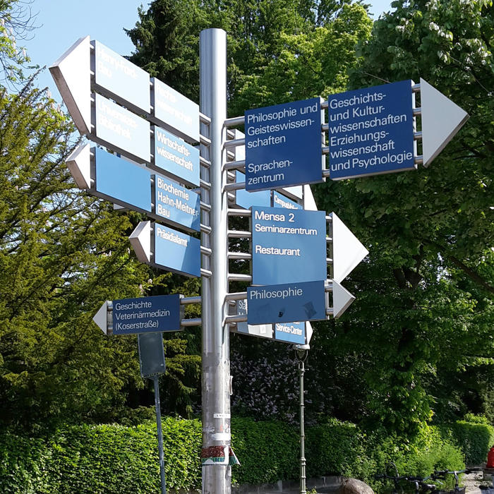 Ein Wegweiser mit mehreren Schildern auf dem Gelände der Freien Universität Berlin.