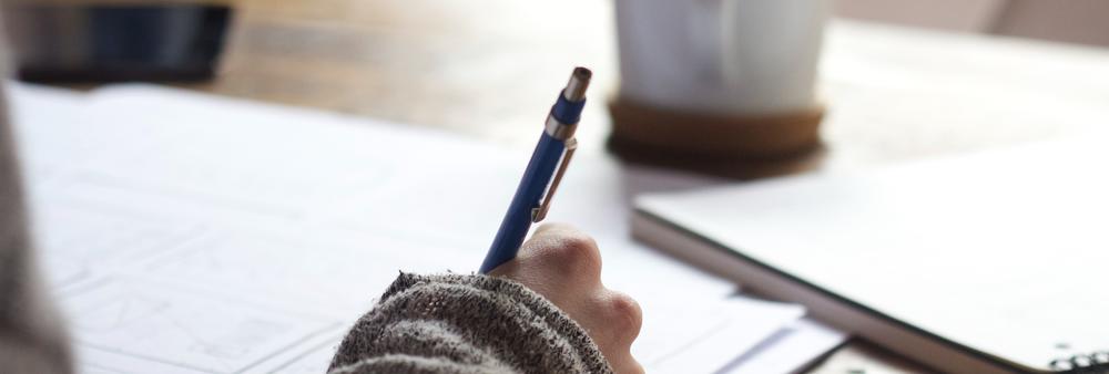 Hand writing with a pen on a piece of paper on wooden table