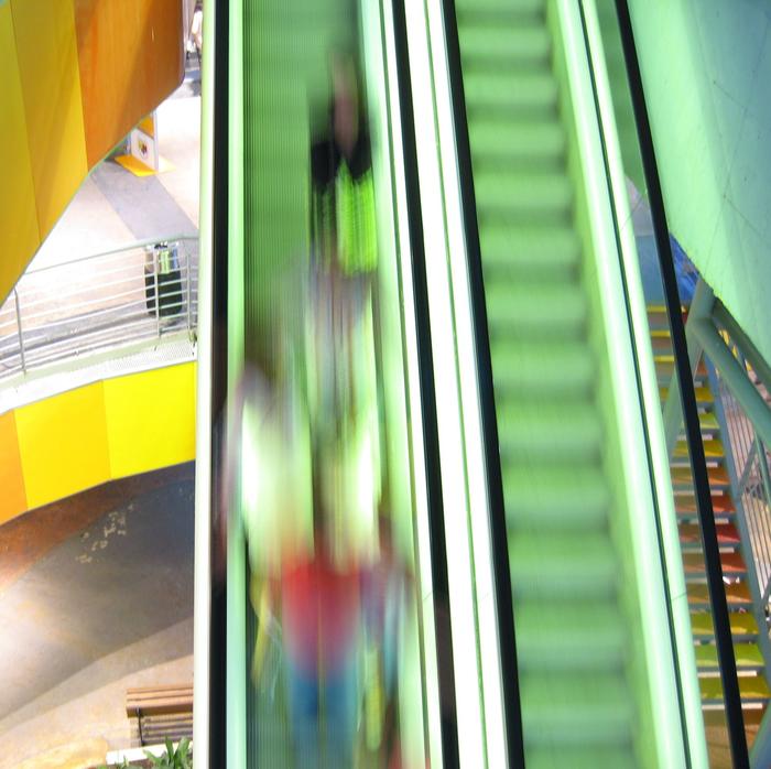 Zwei Rolltreppen. Auf einer Rolltreppe sind verschwommen Menschen zu erkennen.