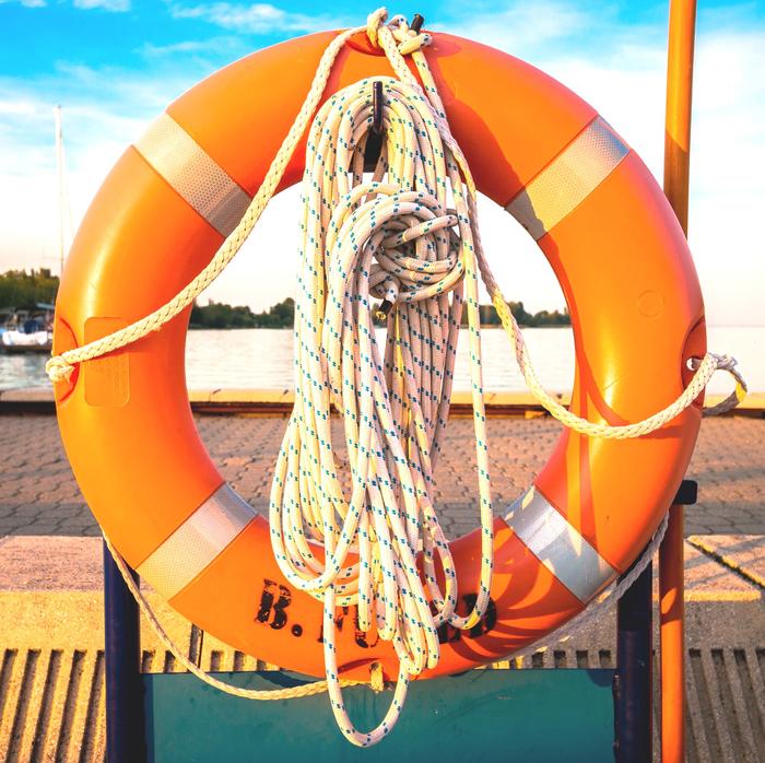 Ein Rettungsring im Vordergrund mit einem Hafen am Meer im Hintergrund.