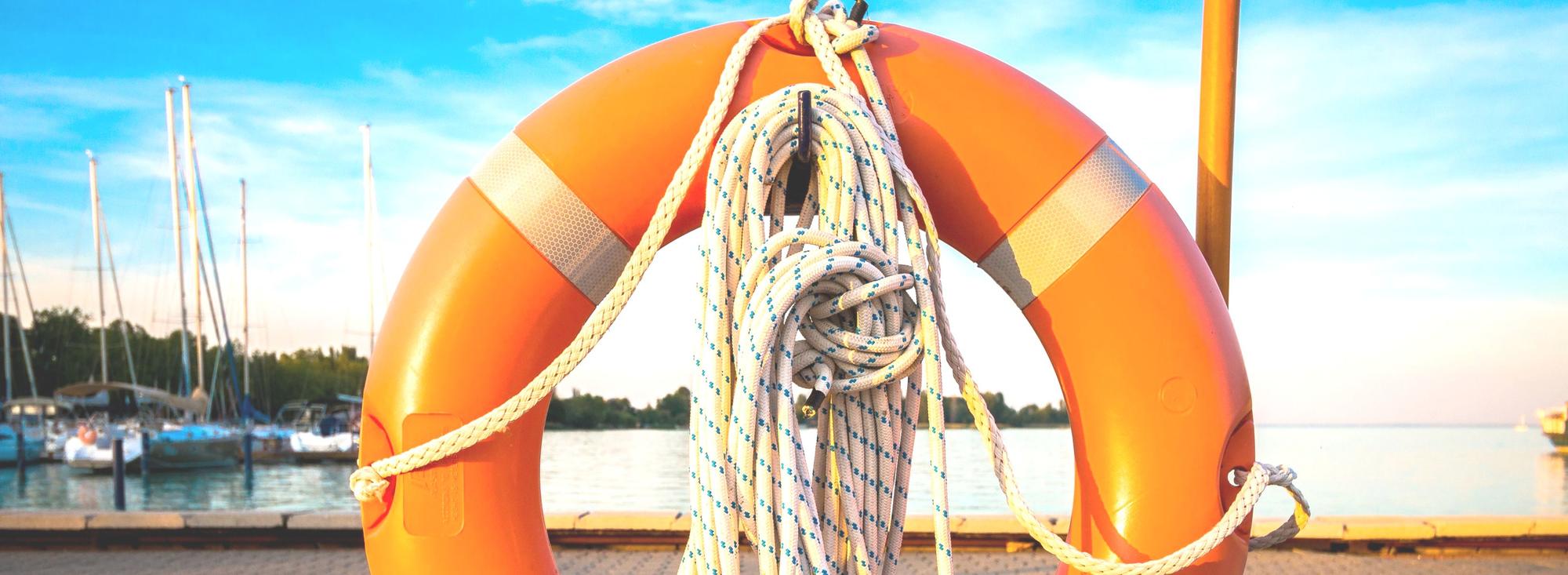 Ein Rettungsring im Vordergrund mit einem Hafen am Meer im Hintergrund.