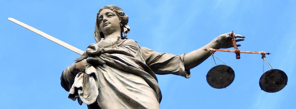 Eine Statue aus Stein hält ein Schwert und eine Waage in ihren Händen. Die Statue ist die Personifikation der Gerechtigkeit, Justitia.