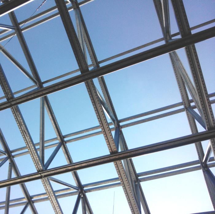 Metal and glass framework of a roof with blue sky in the background.