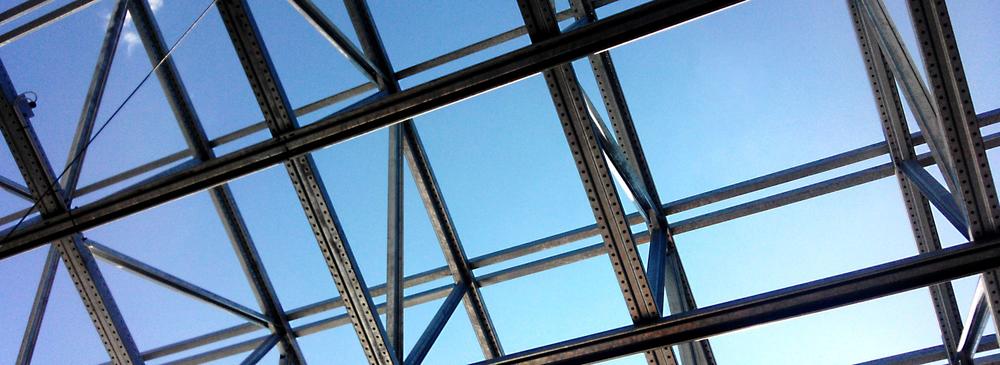 Metal and glass framework of a roof with blue sky in the background.