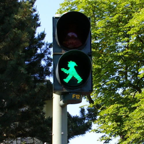 A green pedestrian signal. In the background there are trees with full green foliage.