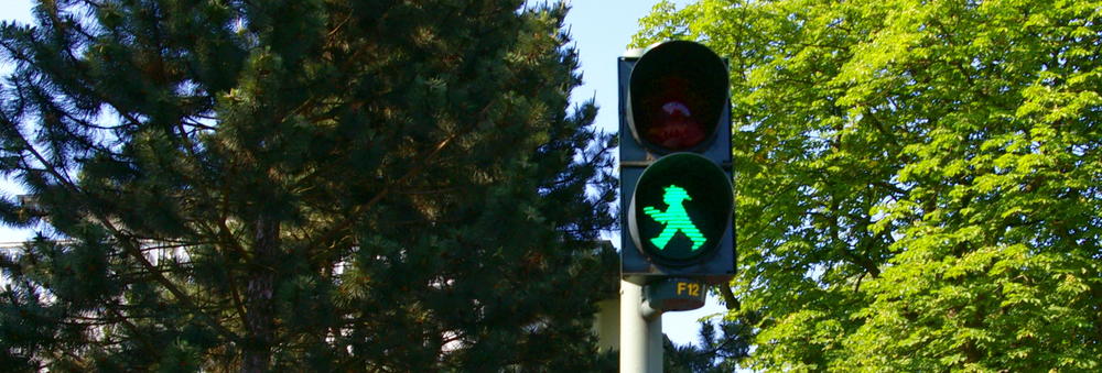 A green pedestrian signal. In the background there are trees with full green foliage.