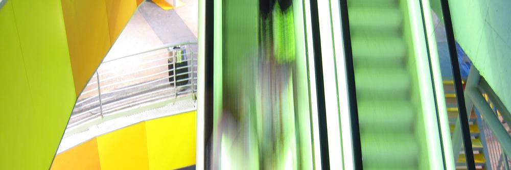 Zwei Rolltreppen. Auf einer Rolltreppe sind verschwommen Menschen zu erkennen.